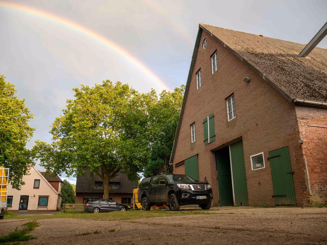 Backsteinscheune mit grünen Toren auf dem Hof, darüber ein Regenbogen